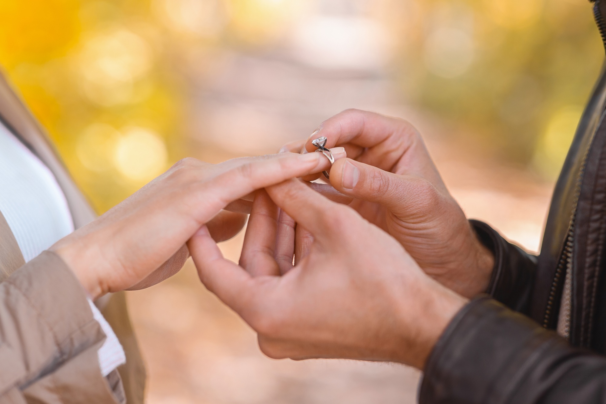 Man putting engagement ring on woman's hand outdoors