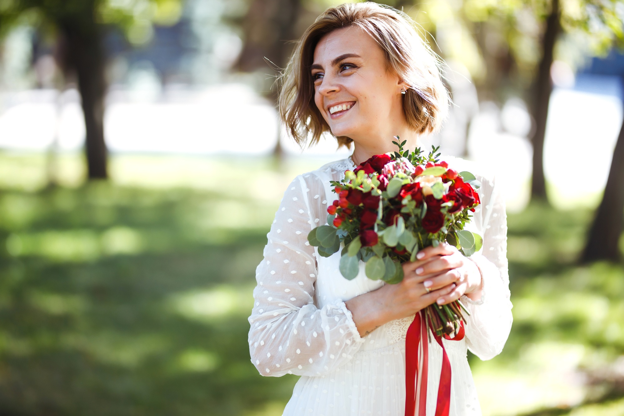 Beautiful bride with wedding bouquet in park. Elegant woman with professional make up and hair style