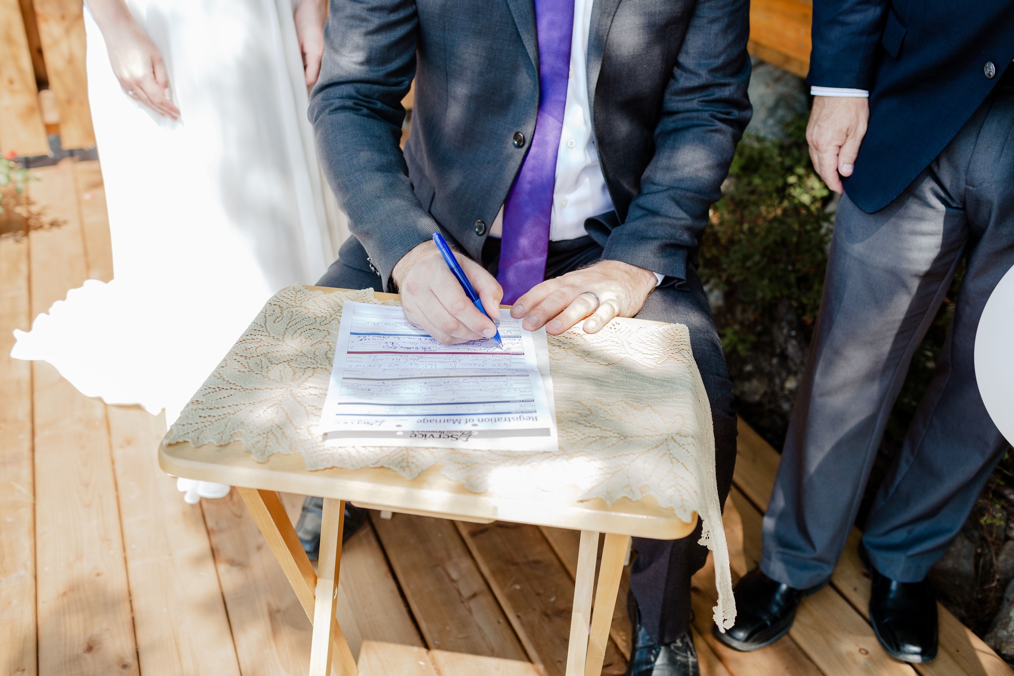 Closeup shot of a groom signing a wedding contract papers on a wooden table on a sunny day