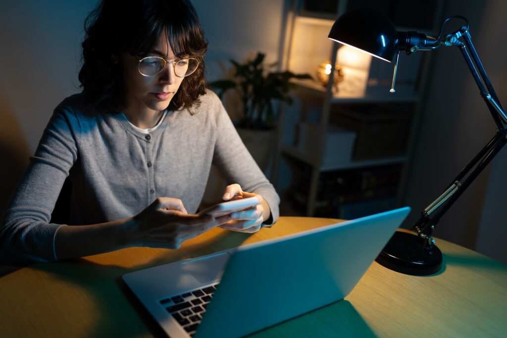 High angle view of woman working late at night using phone, sending text message.