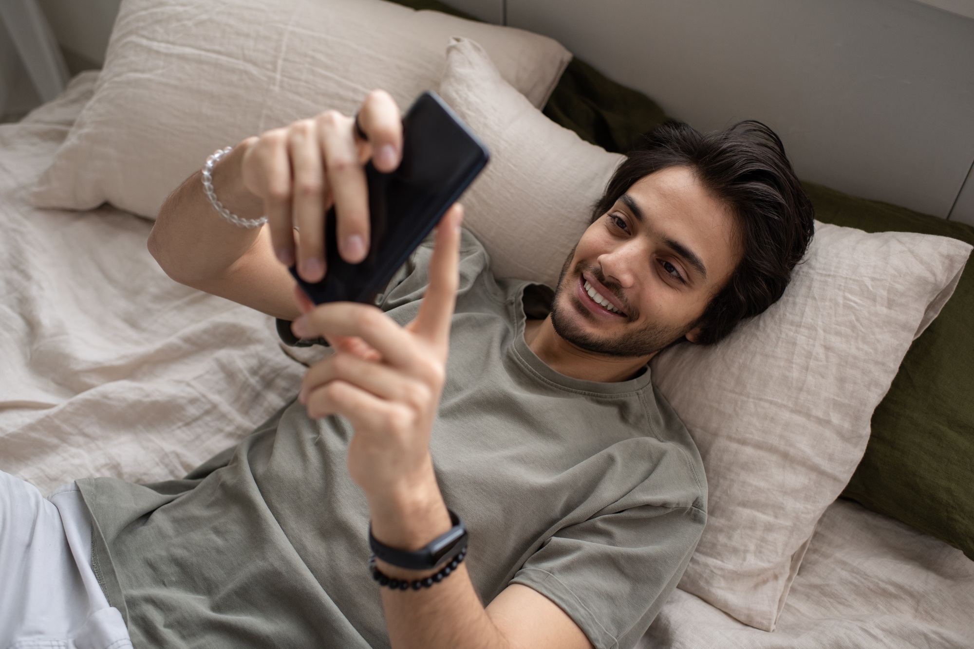 Young manager in grey t-shirt texting in smartphone while lying on bed